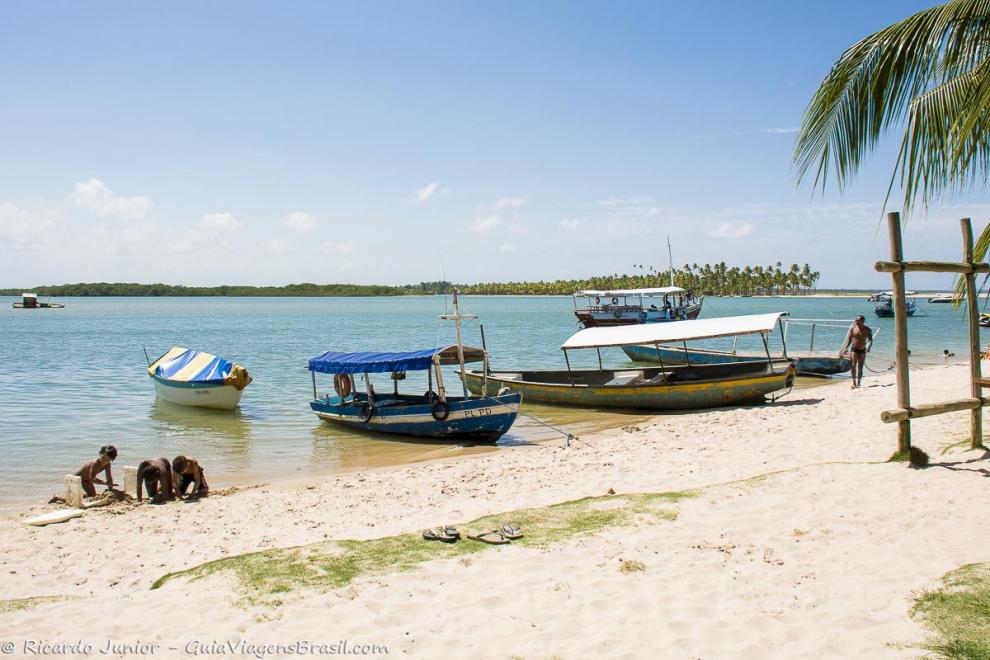 Imagem de crianças brincando na areia e barcos de pescadores.